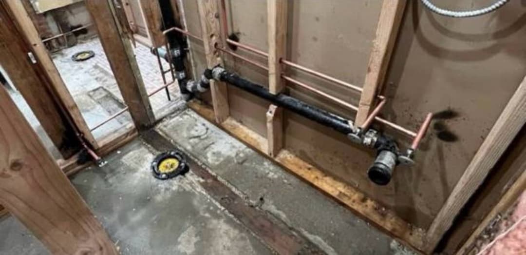 Underfloor plumbing installation showing new drain and supply lines beneath subfloor